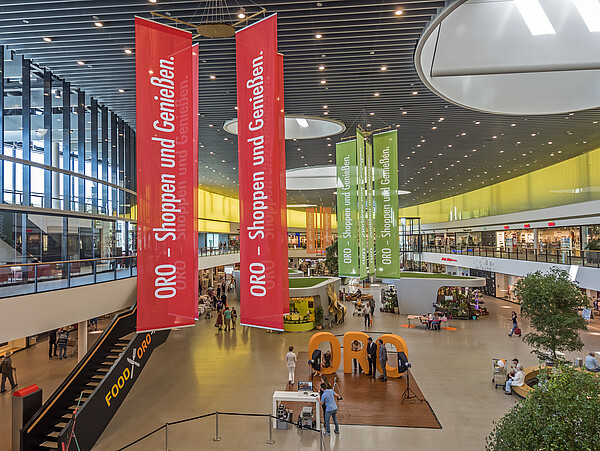Shoppingfreude im ORO Schwabach: Gebäudeautomation von Kieback&Peter sorgt im Hintergrund dafür, dass sich die Besucher wohlfühlen. Innenansicht der Shopping Mall. Großes, lichtdurchflutetes, modernes Gebäude mit Ladengeschäften, Ständen, Banner und vielem mehr.