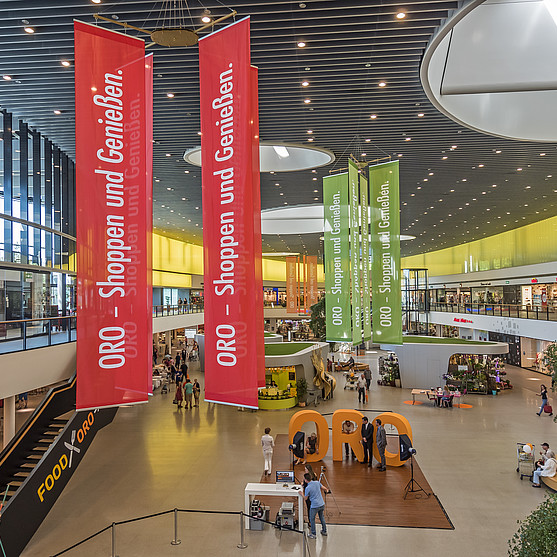 Innenansicht der Shopping Mall. Großes, lichtdurchflutetes, modernes Gebäude mit Ladengeschäften, Ständen, Banner und vielem mehr.