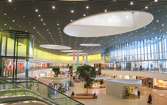 Innenansicht des modernen, hellen Einkaufszentrums mit großen Fenstern, Läden und Ständen.