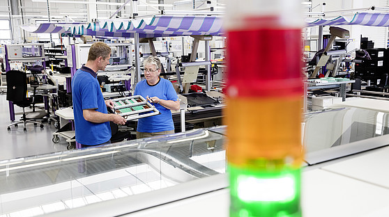 Kieback&Peter Mitarbeiter im Werk Mittenwalde Zwei Mitarbeiter tauschen sich aus. Im Vordergrund sieht man eine grün leuchtende Ampel.