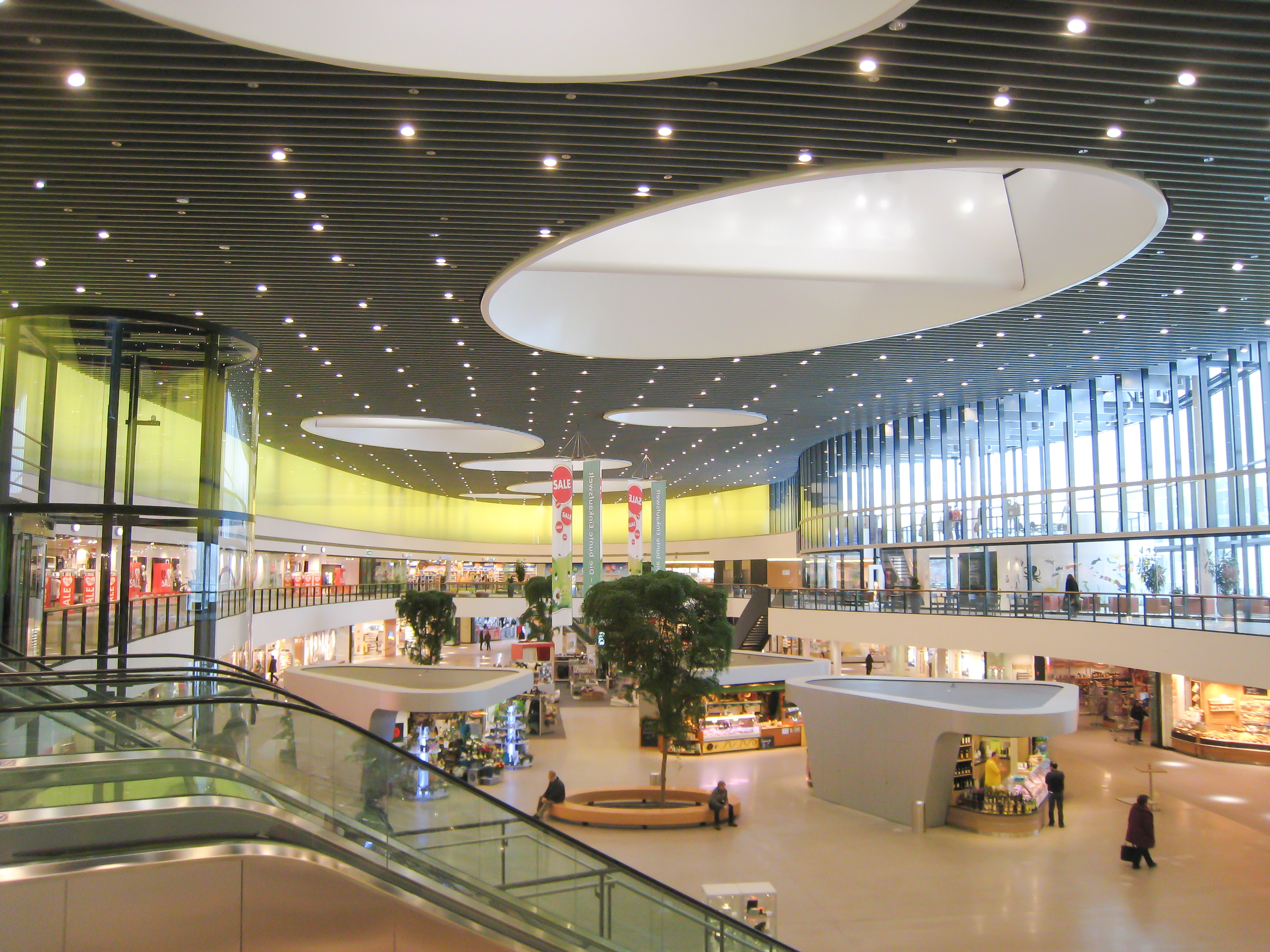 Innenansicht des modernen, hellen Einkaufszentrums mit großen Fenstern, Läden und Ständen.
